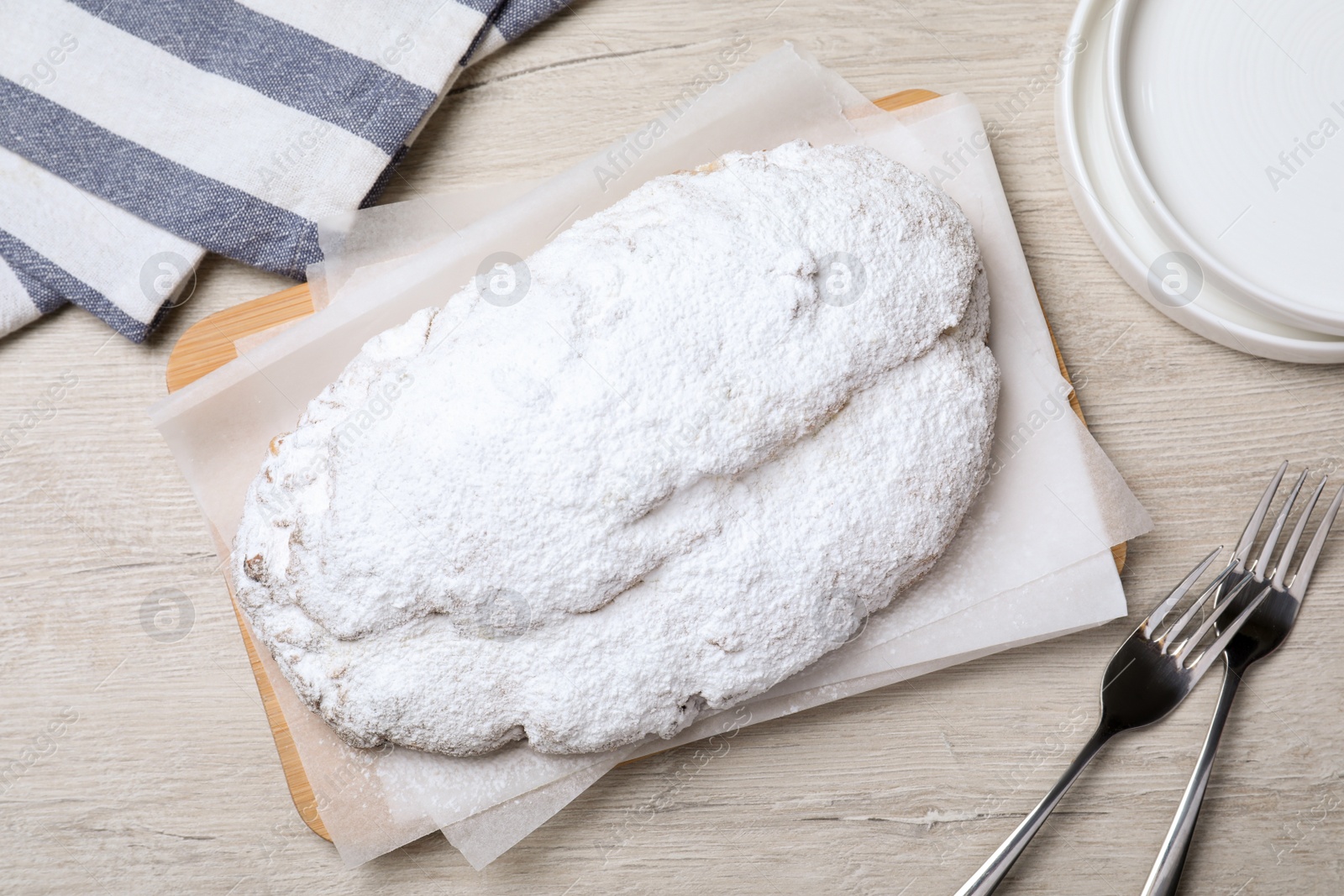 Photo of Delicious Stollen sprinkled with powdered sugar on wooden table, flat lay