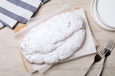 Photo of Delicious Stollen sprinkled with powdered sugar on wooden table, flat lay