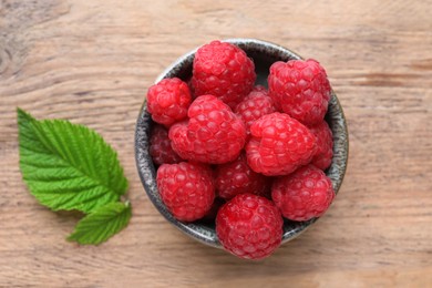 Photo of Tasty ripe raspberries and green leaves on wooden table, top view