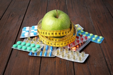 Photo of Weight loss pills and apple with measuring tape on wooden background