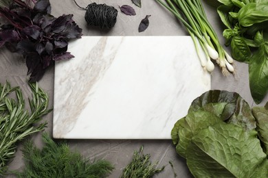 Different herbs and marble cutting board on grey table, flat lay. Space for text