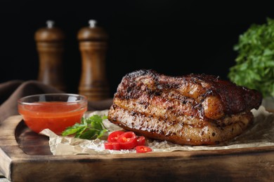 Photo of Piece of baked pork belly served with sauce and chili pepper on wooden board, closeup