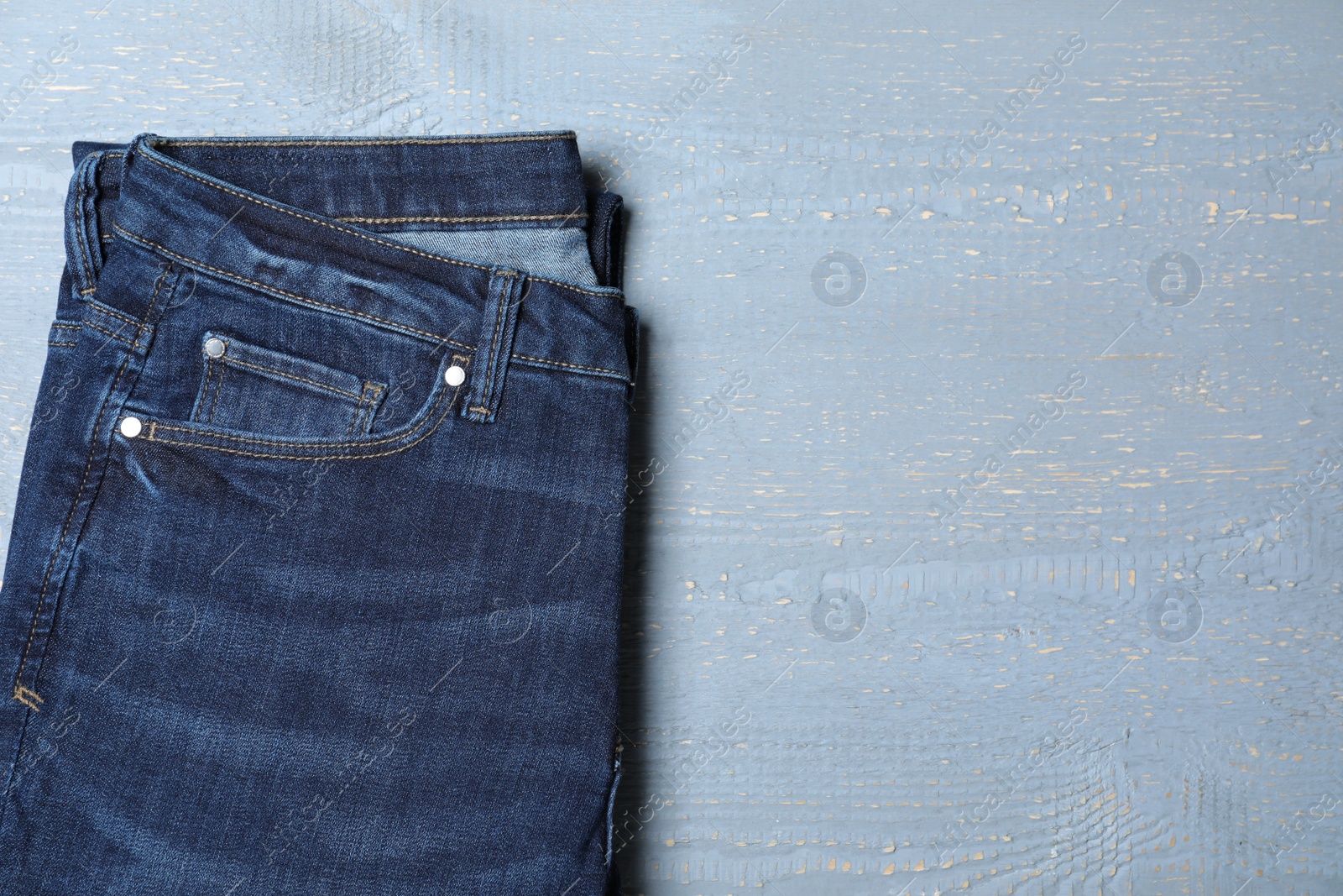 Photo of New stylish jeans on light grey wooden background, top view. Space for text