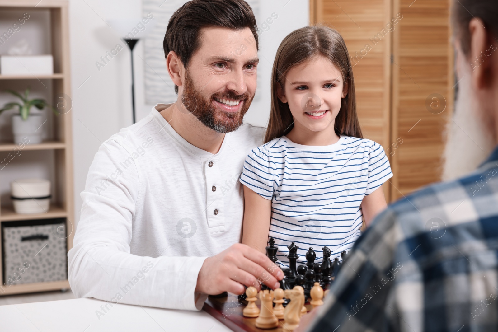 Photo of Family playing chess together at table in room