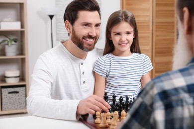 Family playing chess together at table in room