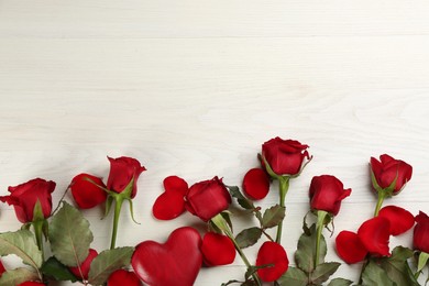 Beautiful red roses and decorative heart on white wooden background, flat lay with space for text. Valentine's Day celebration