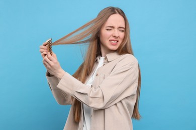 Photo of Emotional woman brushing her hair on light blue background. Alopecia problem