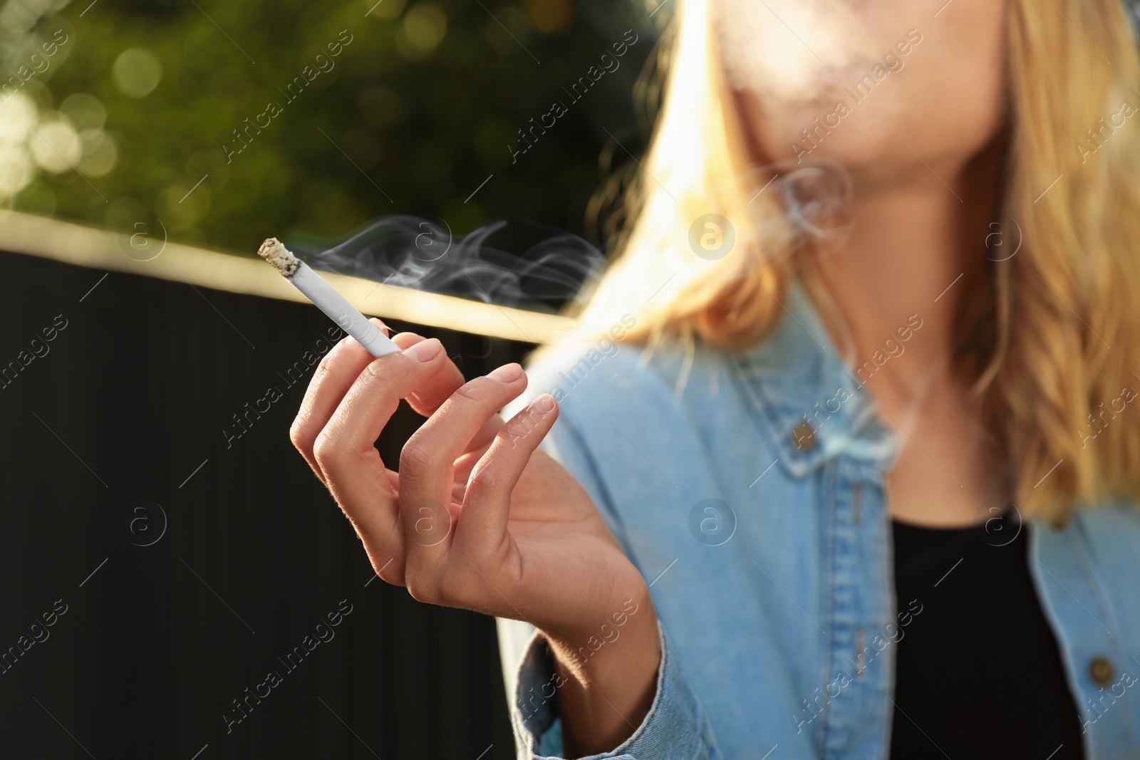 Photo of Young woman smoking cigarette outdoors, closeup view