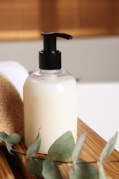 Photo of Dispenser of liquid soap and eucalyptus branch on wooden table