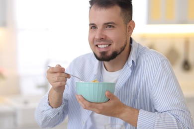 Smiling man eating tasty cornflakes at breakfast indoors