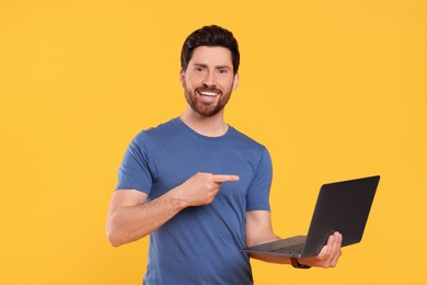 Photo of Happy man with laptop pointing at something on yellow background