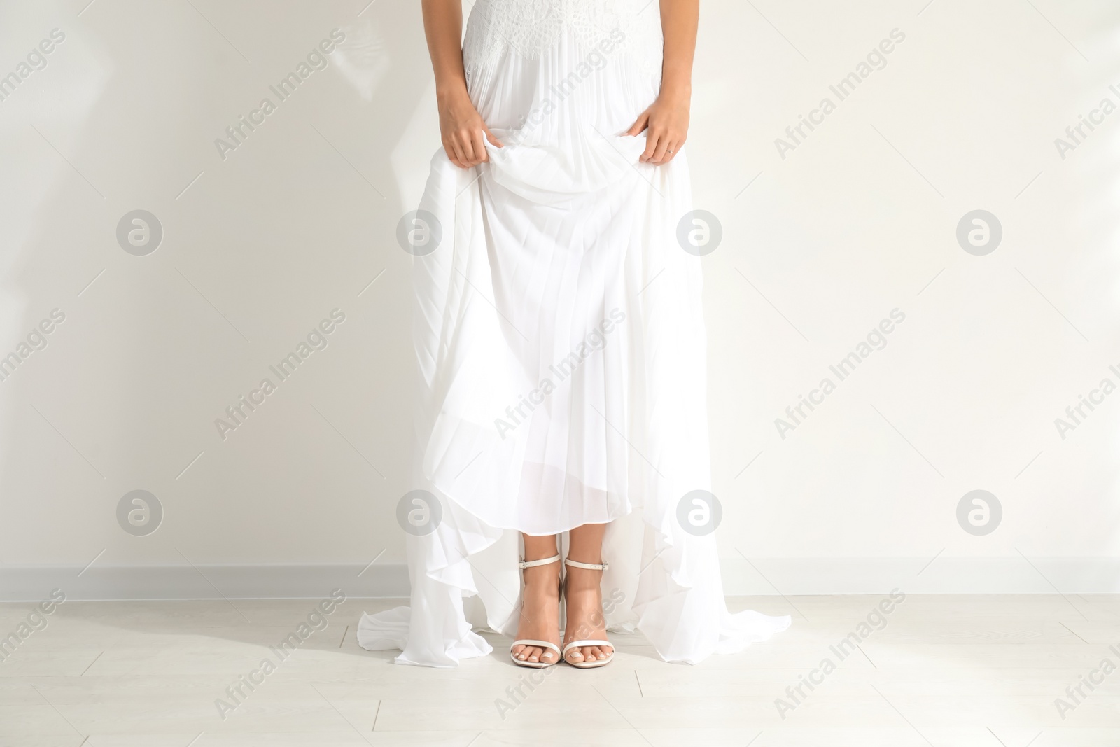 Photo of Young bride wearing beautiful wedding dress near light wall, closeup