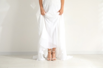 Young bride wearing beautiful wedding dress near light wall, closeup