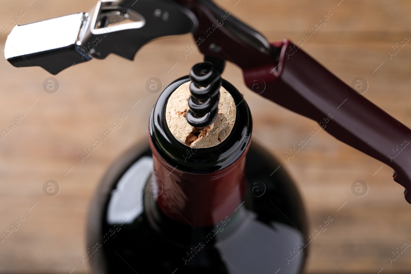 Photo of Opening wine bottle with corkscrew on blurred background, closeup