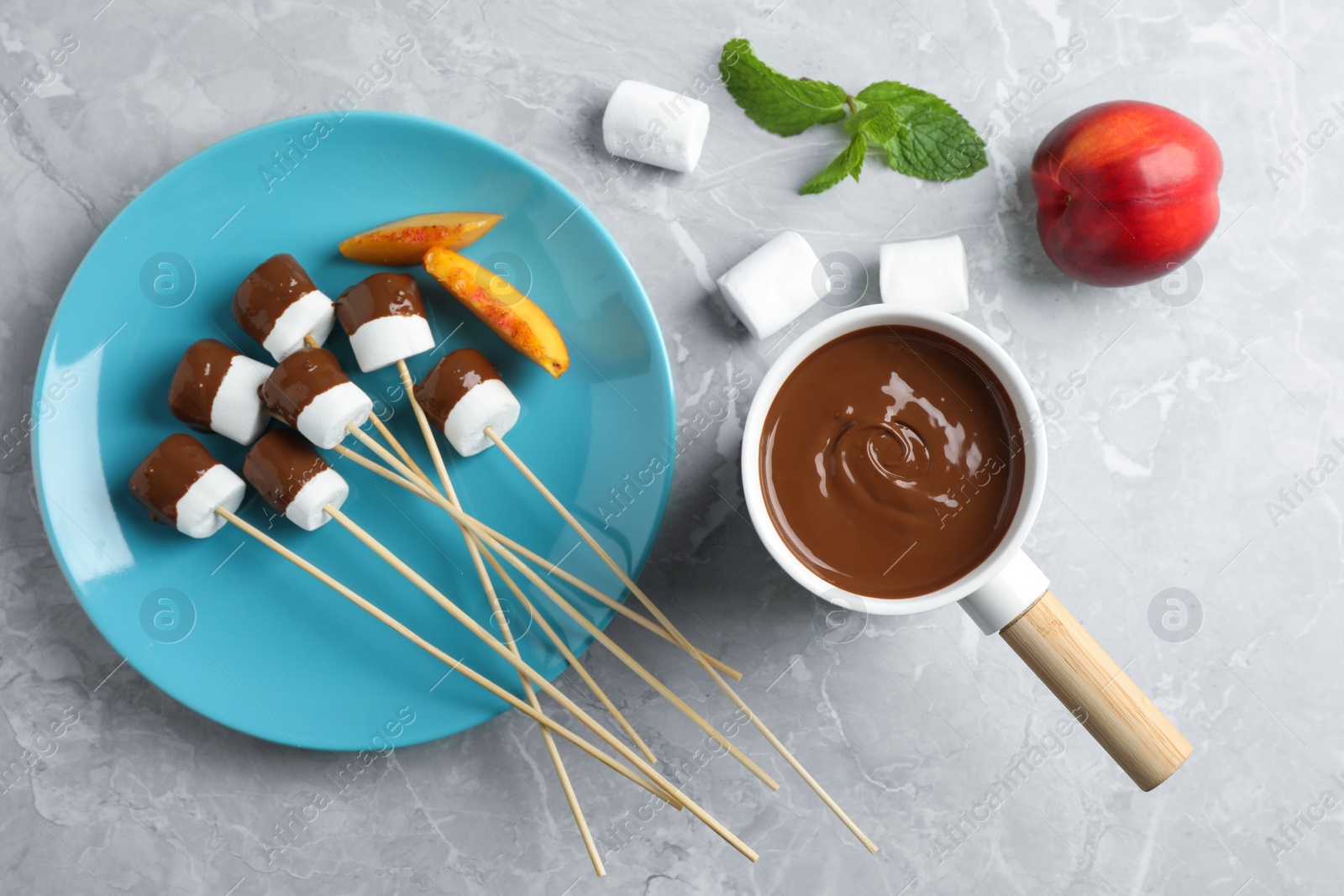 Photo of Fondue pot with milk chocolate and marshmallows on marble table, top view