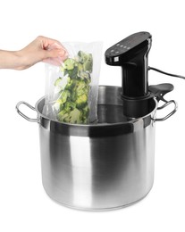 Photo of Woman putting vacuum packed broccoli into pot with sous vide cooker on white background, closeup. Thermal immersion circulator