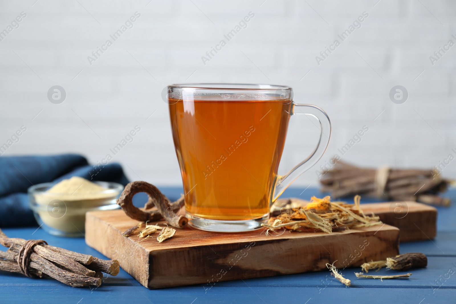 Photo of Aromatic licorice tea in cup and dried sticks of licorice root on blue wooden table