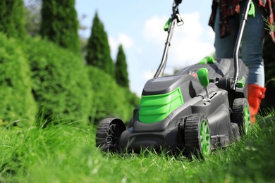 Photo of Woman cutting grass with lawn mower in garden on sunny day, closeup