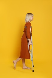 Photo of Full length portrait of woman with crutches on yellow background