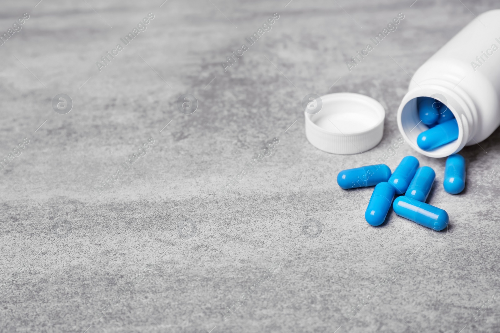 Photo of Container with blue capsules on grey background