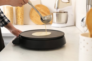 Photo of Man cooking delicious crepe on electric pancake maker in kitchen, closeup
