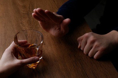 Photo of Man refusing to drink whiskey at wooden table, closeup. Alcohol addiction treatment