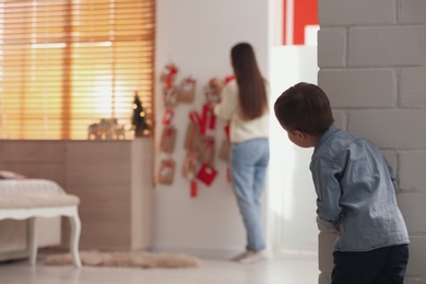 Photo of Little boy watching his mother taking gift from Advent calendar at home, back view. Christmas tradition