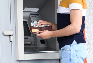 Man with money near cash machine outdoors, closeup