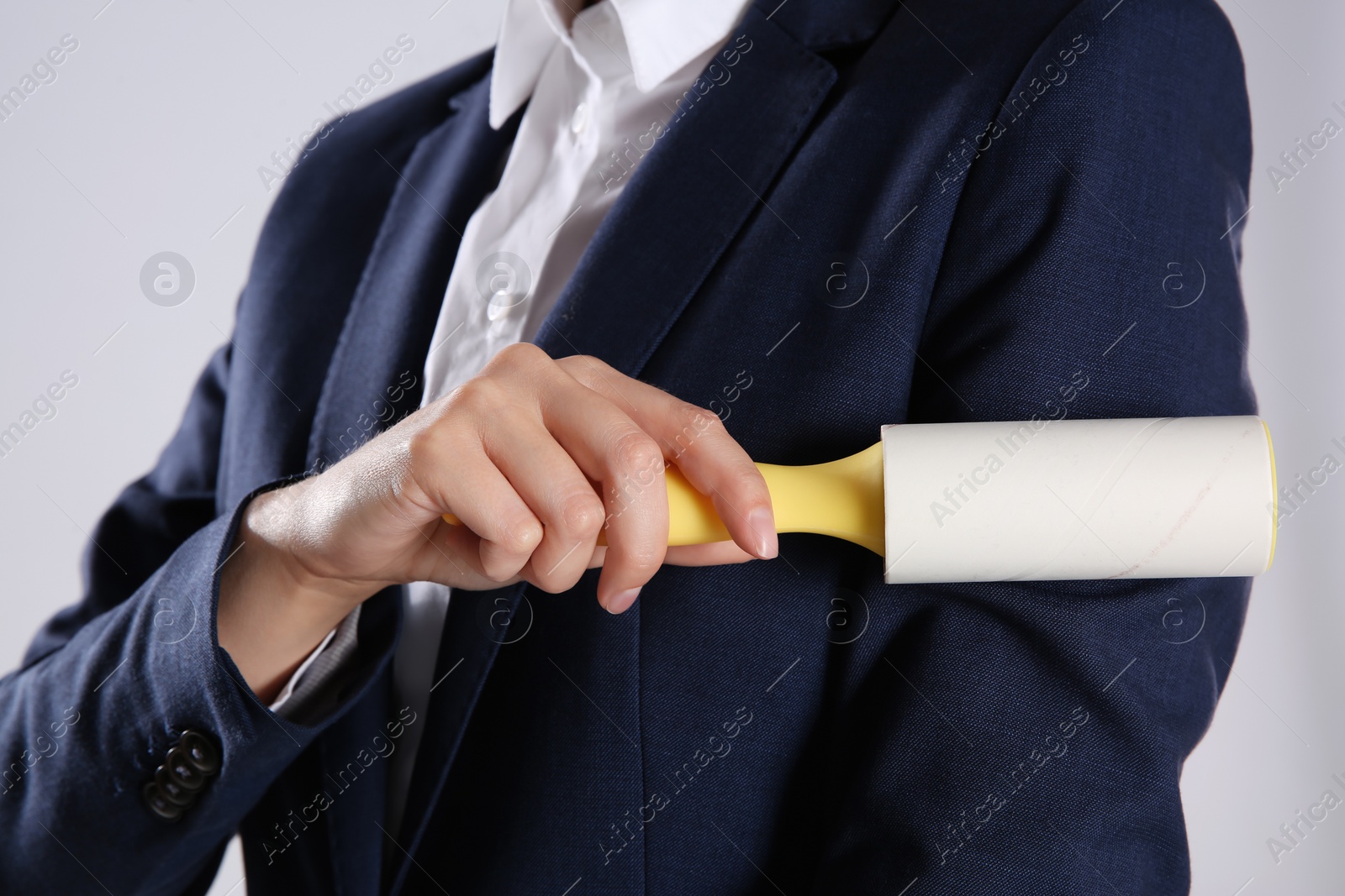 Photo of Woman cleaning dark blue jacket with lint roller on grey background, closeup