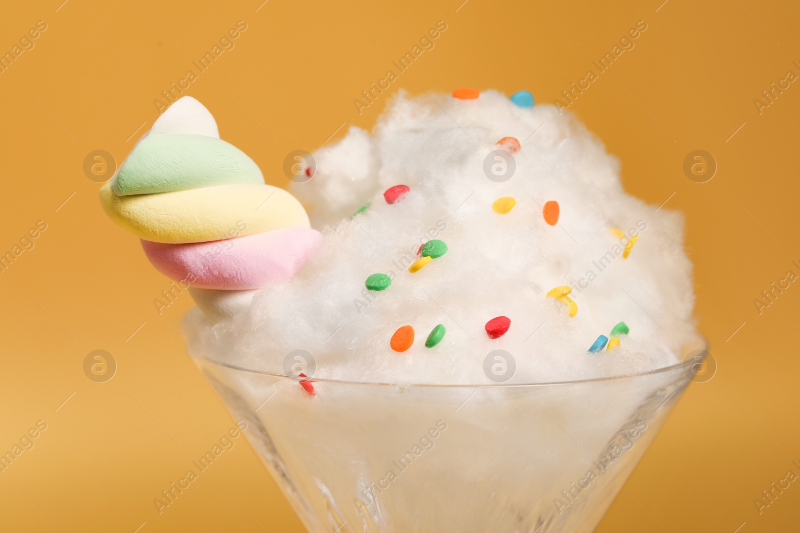 Photo of Martini glass with cotton, sprinkles and marshmallow on yellow background, closeup