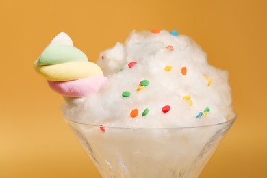 Martini glass with cotton, sprinkles and marshmallow on yellow background, closeup