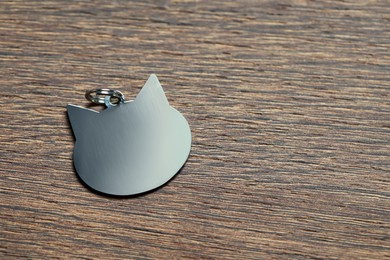 Photo of Silver pet tag in shape of cat on wooden table, top view. Space for text