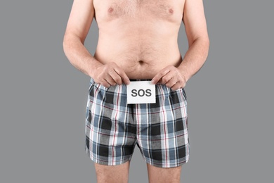 Photo of Mature man with urological problems holding SOS sign on grey background