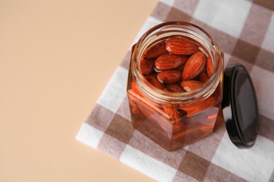 Photo of Jar with almonds and honey on beige table, space for text