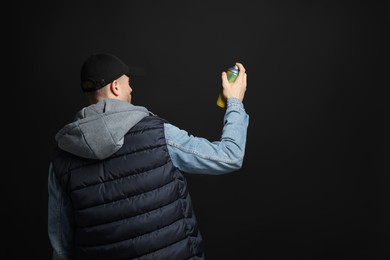 Man holding used can of spray paint on black background, back view. Space for text