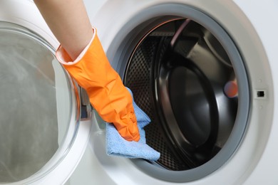 Photo of Woman cleaning empty washing machine with rag, closeup