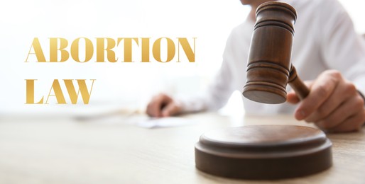 Image of Abortion law. Judge with gavel at wooden table indoors, closeup. Banner design