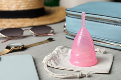 Pink menstrual cup with cotton bag and women's accessories on white wooden table