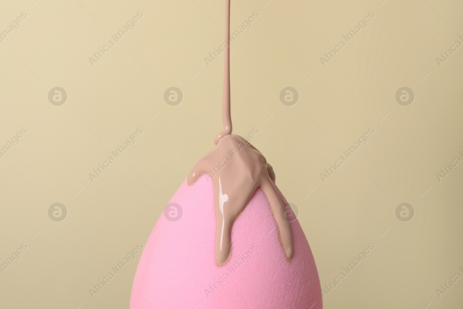 Photo of Skin foundation pouring onto makeup sponge on beige background