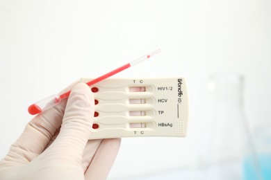 Photo of Doctor holding disposable express test for hepatitis and pipette with blood indoors, closeup