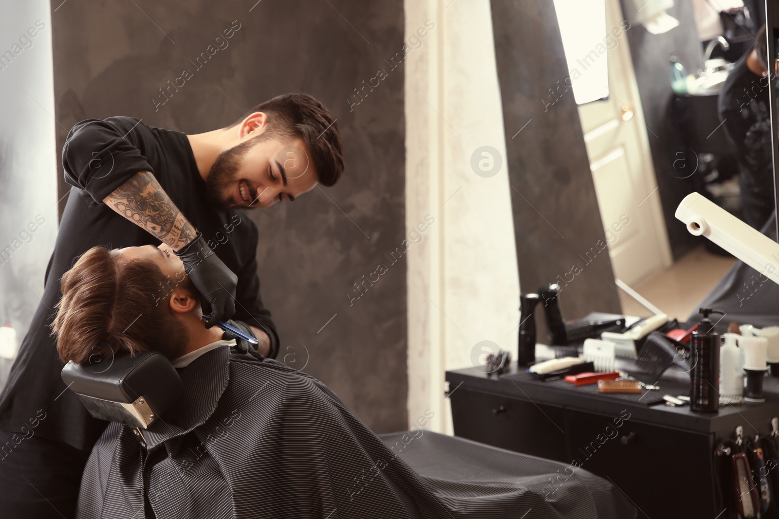 Photo of Professional hairdresser shaving client with straight razor in barbershop