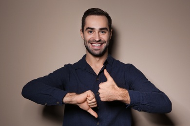 Photo of Man showing THUMB UP and DOWN gesture in sign language on color background