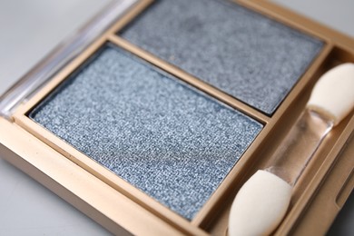 Beautiful eyeshadow palette with applicator on light gray background, closeup. Professional cosmetic product