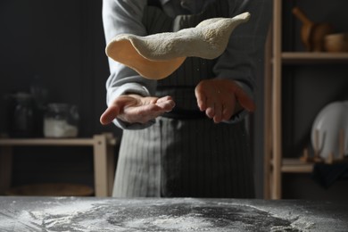 Woman tossing pizza dough at table in kitchen, closeup