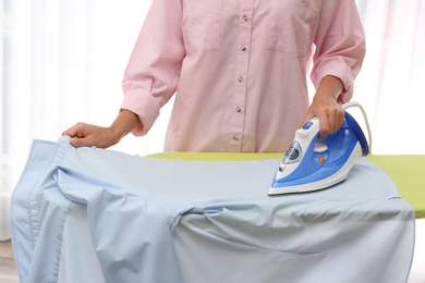 Photo of Young woman ironing clean shirt at home, closeup. Laundry day