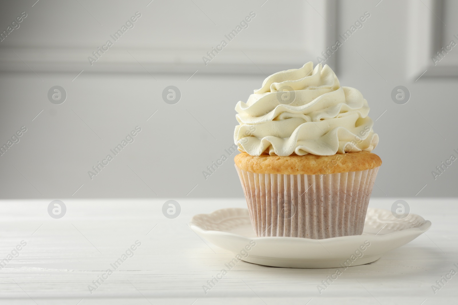 Photo of Tasty vanilla cupcake with cream on white table, closeup. Space for text