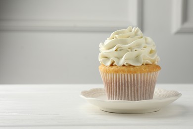 Tasty vanilla cupcake with cream on white table, closeup. Space for text