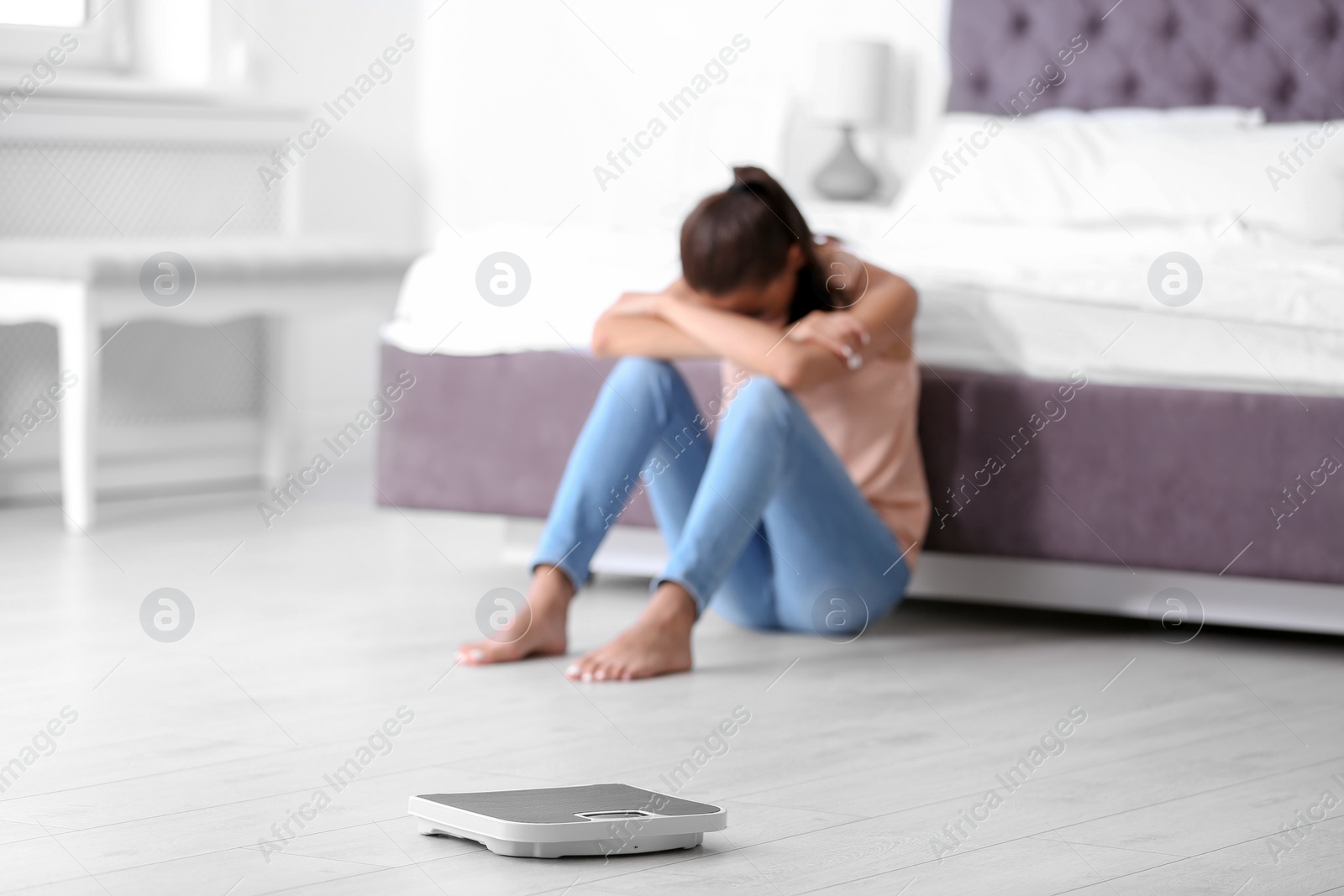 Photo of Scales on floor and sad young woman at home. Weight loss motivation