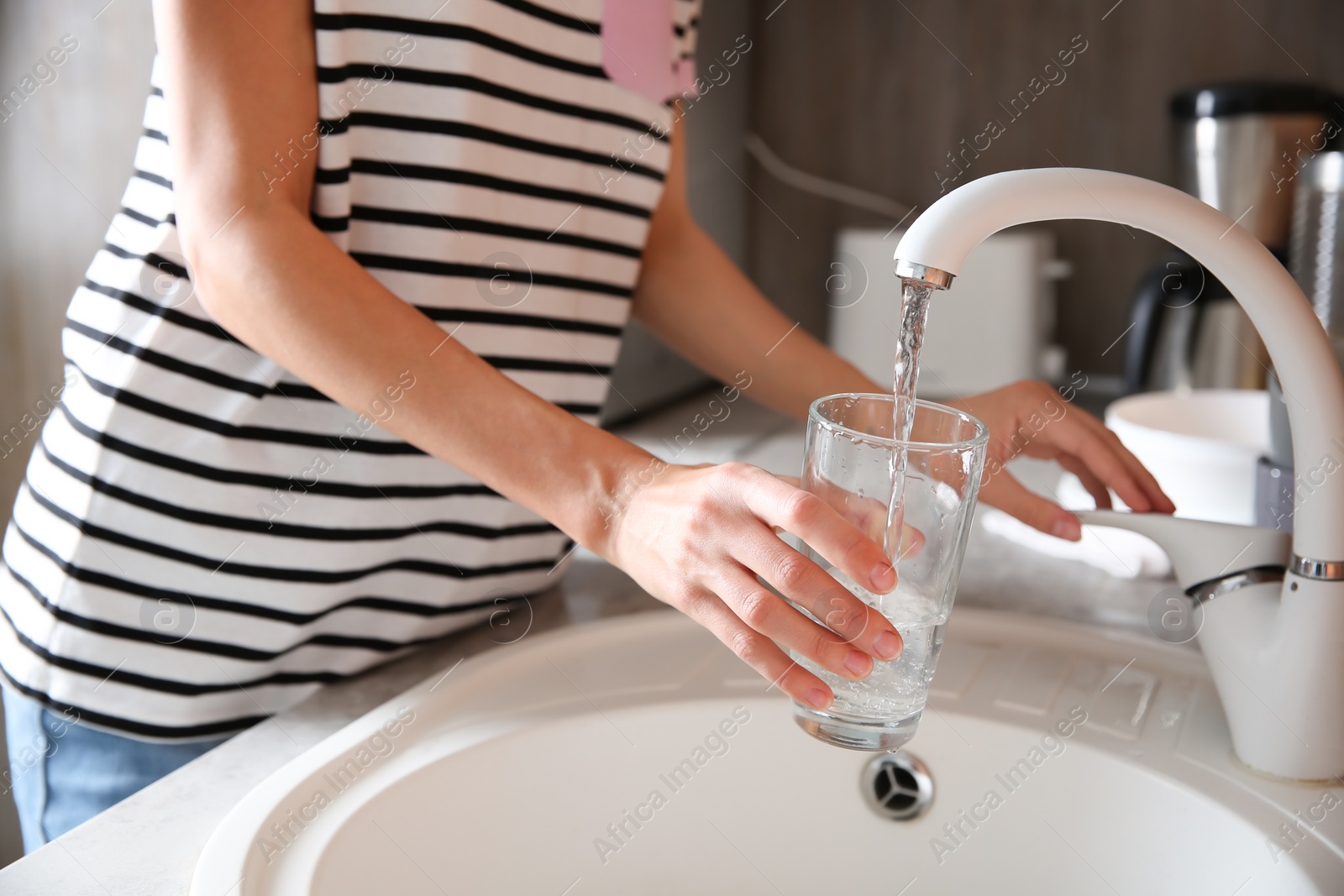 Photo of Woman filling glass with water from faucet in kitchen, closeup