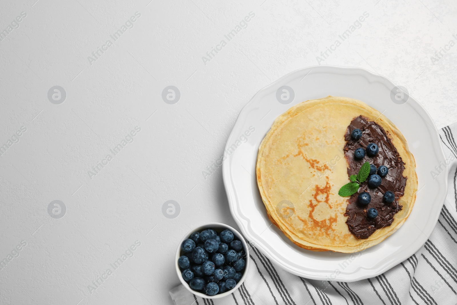 Photo of Delicious crepes with fresh berries and chocolate on white table, flat lay. Space for text